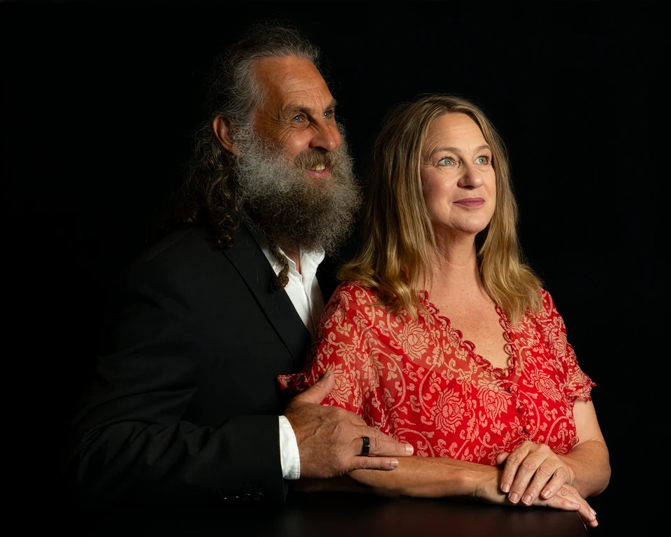 Deb and Ian together against a dark backdrop, both looking off to one side, Ian smiling.