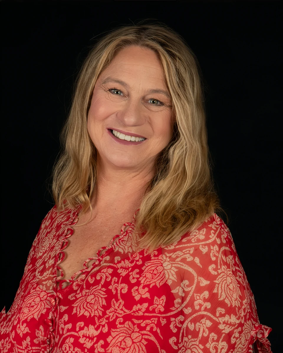 Deb against a dark backdrop in a red patterned top, smiling towards the camera.